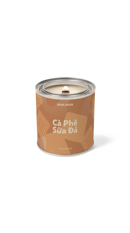 A single cylindrical candle tin on a plain white background. The tin is brown with lighter brown chocolate chip illustrations and white text reading 'BASK HOUR' and 'Câ Phé Sùra Dá'.