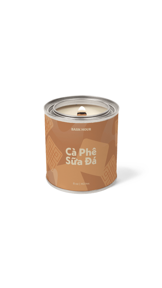 A single cylindrical candle tin on a plain white background. The tin is brown with lighter brown chocolate chip illustrations and white text reading 'BASK HOUR' and 'Câ Phé Sùra Dá'.